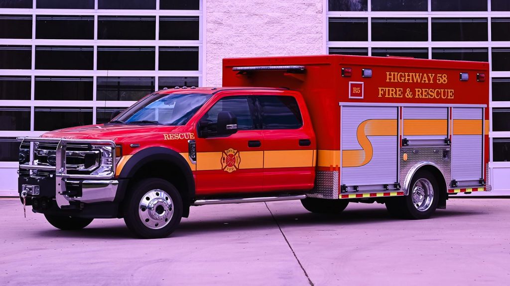 A red and yellow rescue vehicle from Highway 58 Fire & Rescue is parked in front of a building with large glass doors. The vehicle is equipped with various compartments and emergency lights, featuring the fire department's emblem on the side.